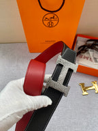 Hermes belt with black textured leather strap, gold-tone H buckle, red inner panel.