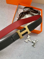 Hermes belt close-up with gold-tone H buckle, black textured leather and red strap side.