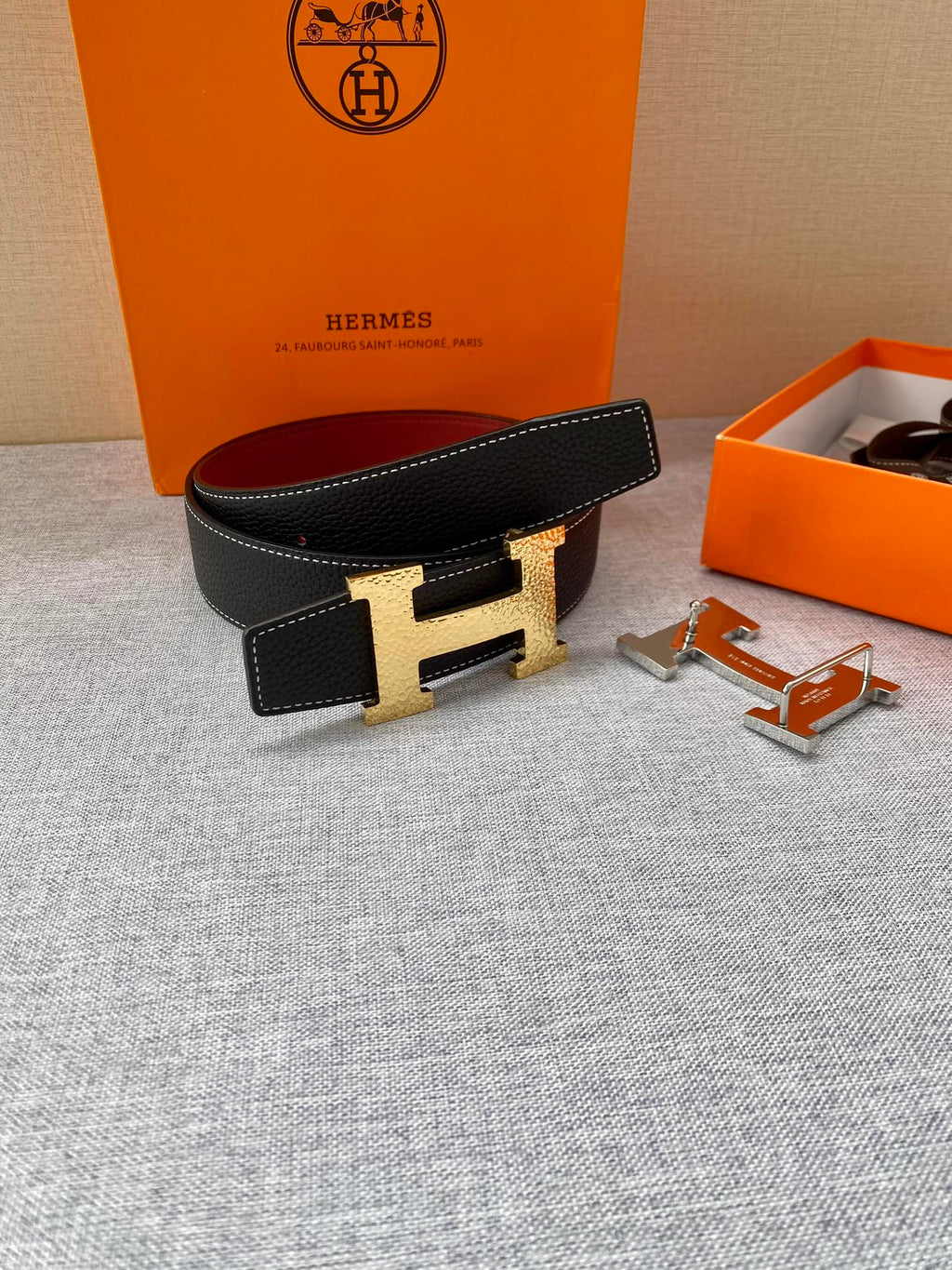 Hermes belt on display: black textured leather, gold-tone H buckle, red lining, with accessories.
