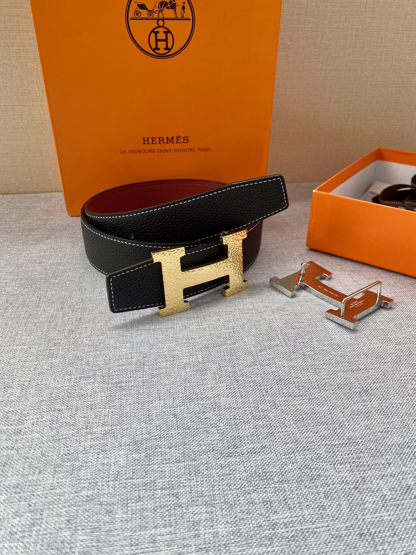 Hermes belt on display: black textured leather, gold-tone H buckle, red lining, with accessories.