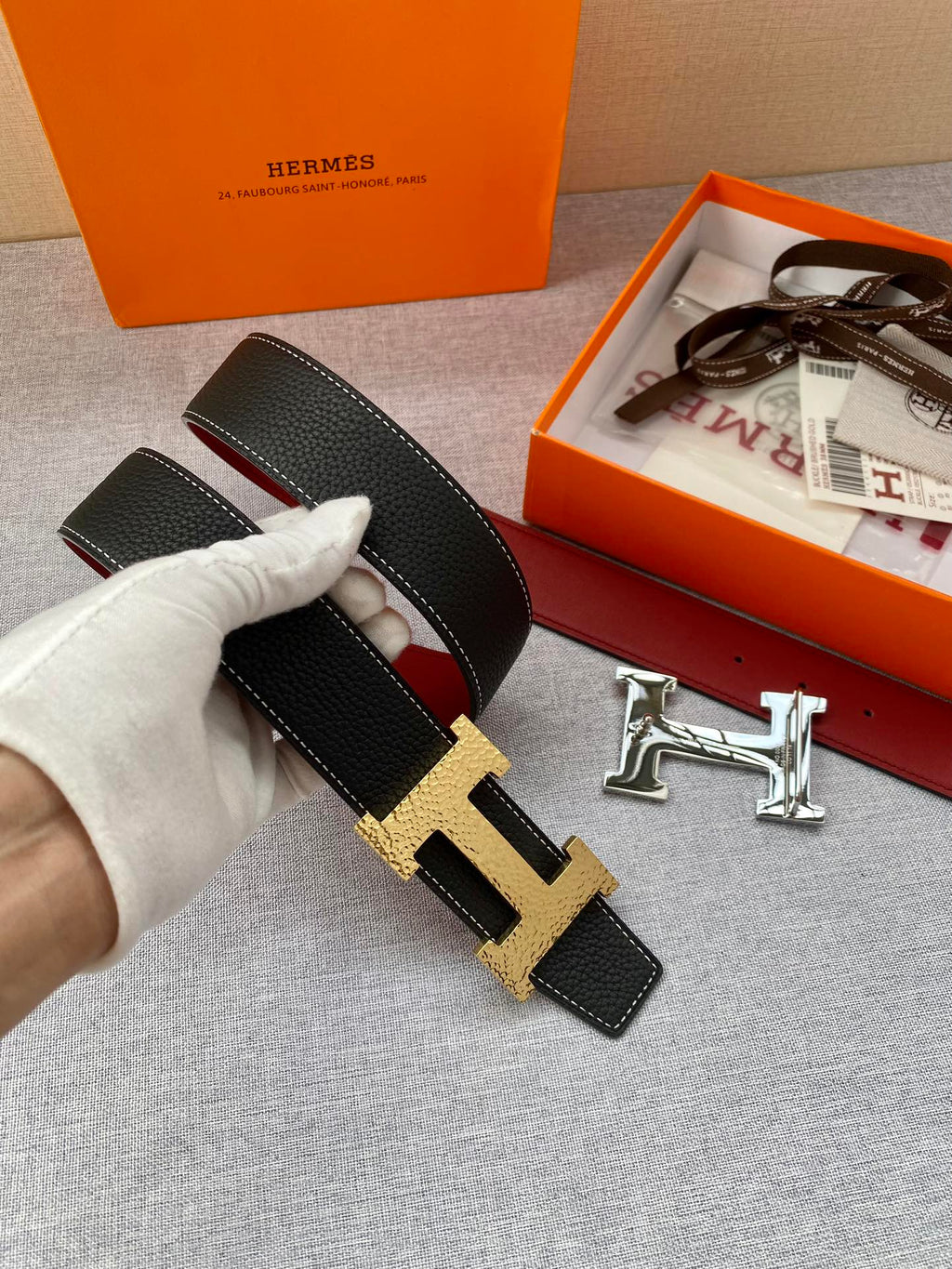 Hermes belt close-up held in hand: black textured leather with gold-tone H buckle.