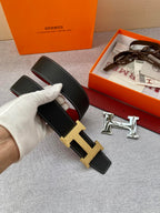 Hermes belt close-up held in hand: black textured leather with gold-tone H buckle.