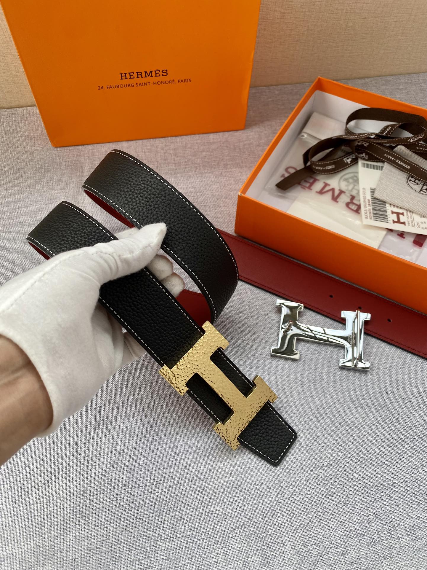Hermes belt close-up held in hand: black textured leather with gold-tone H buckle.