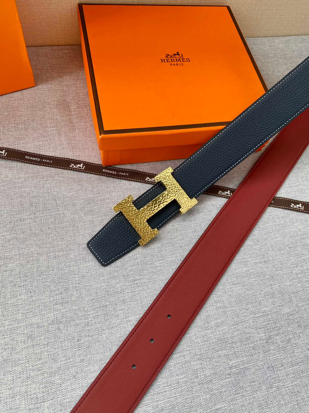 Hermes dark blue leather belt with gold H buckle and red underside strap.
