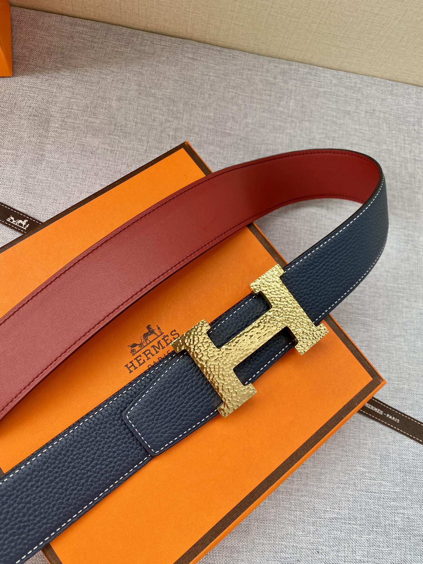 Navy leather belt with gold-tone H buckle, red underside lining visible