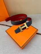 Navy leather belt with gold-tone H buckle, folded beside orange box