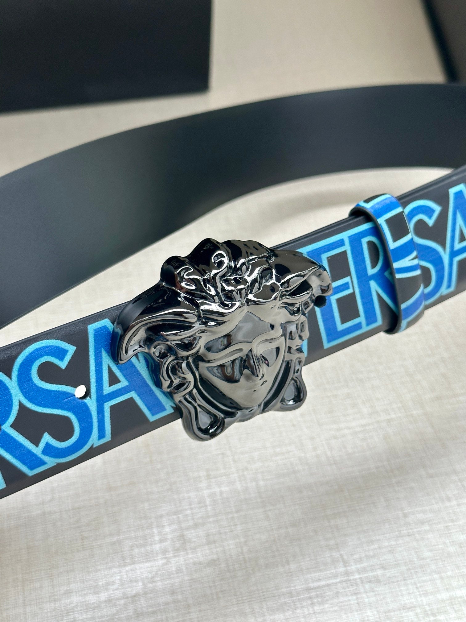 Silver lion buckle with black belt strap featuring blue VERSACE lettering