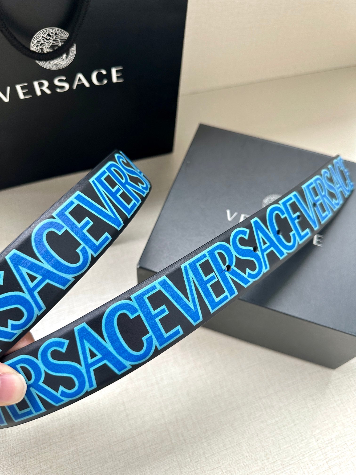 Belt strap close-up with blue repeating VERSACE lettering and black base