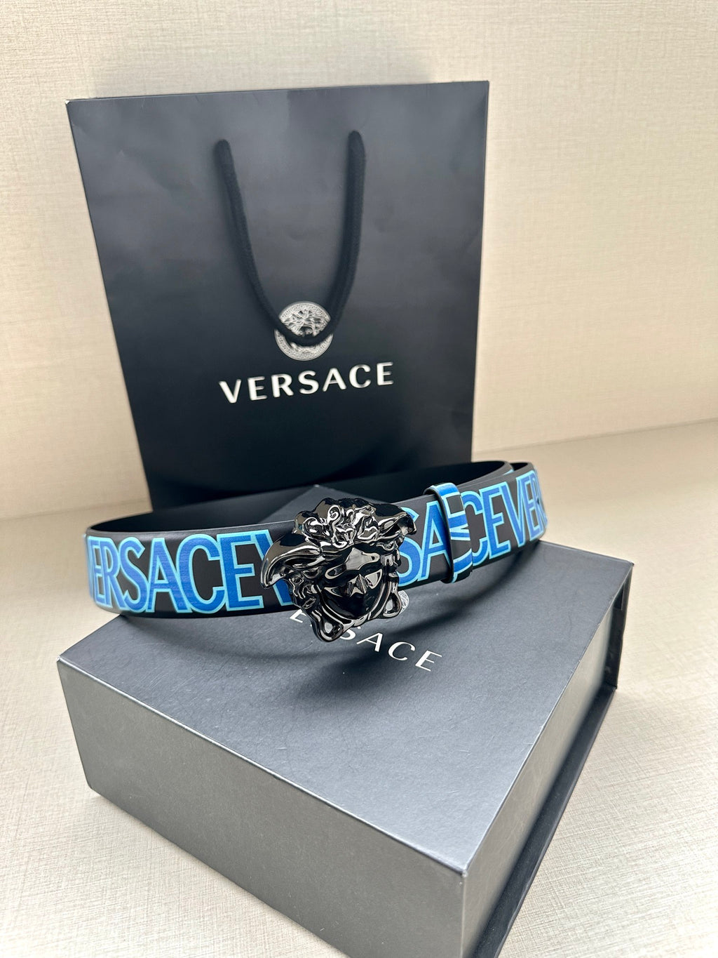 Designer belt on gray box, blue repeating VERSACE strap and silver lion buckle