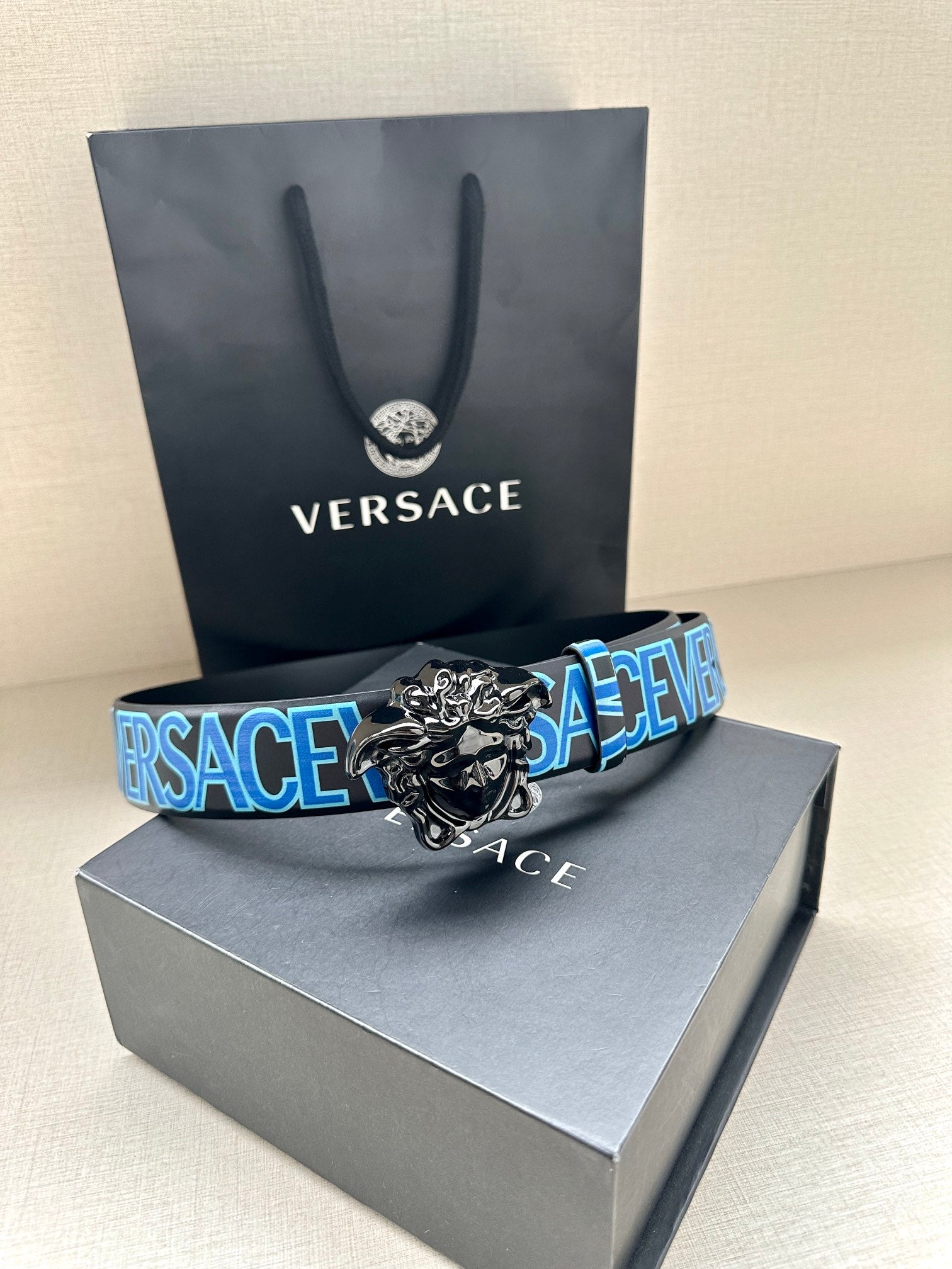 Designer belt on gray box, blue repeating VERSACE strap and silver lion buckle