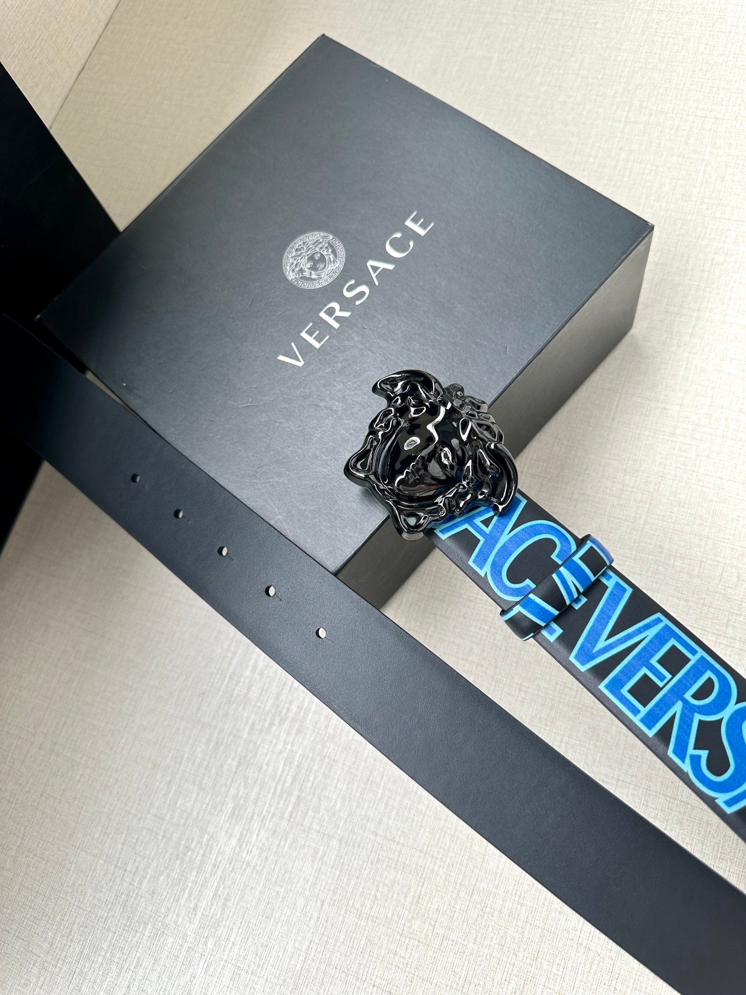 Designer belt on gray gift box, blue logo strap with ornate silver buckle