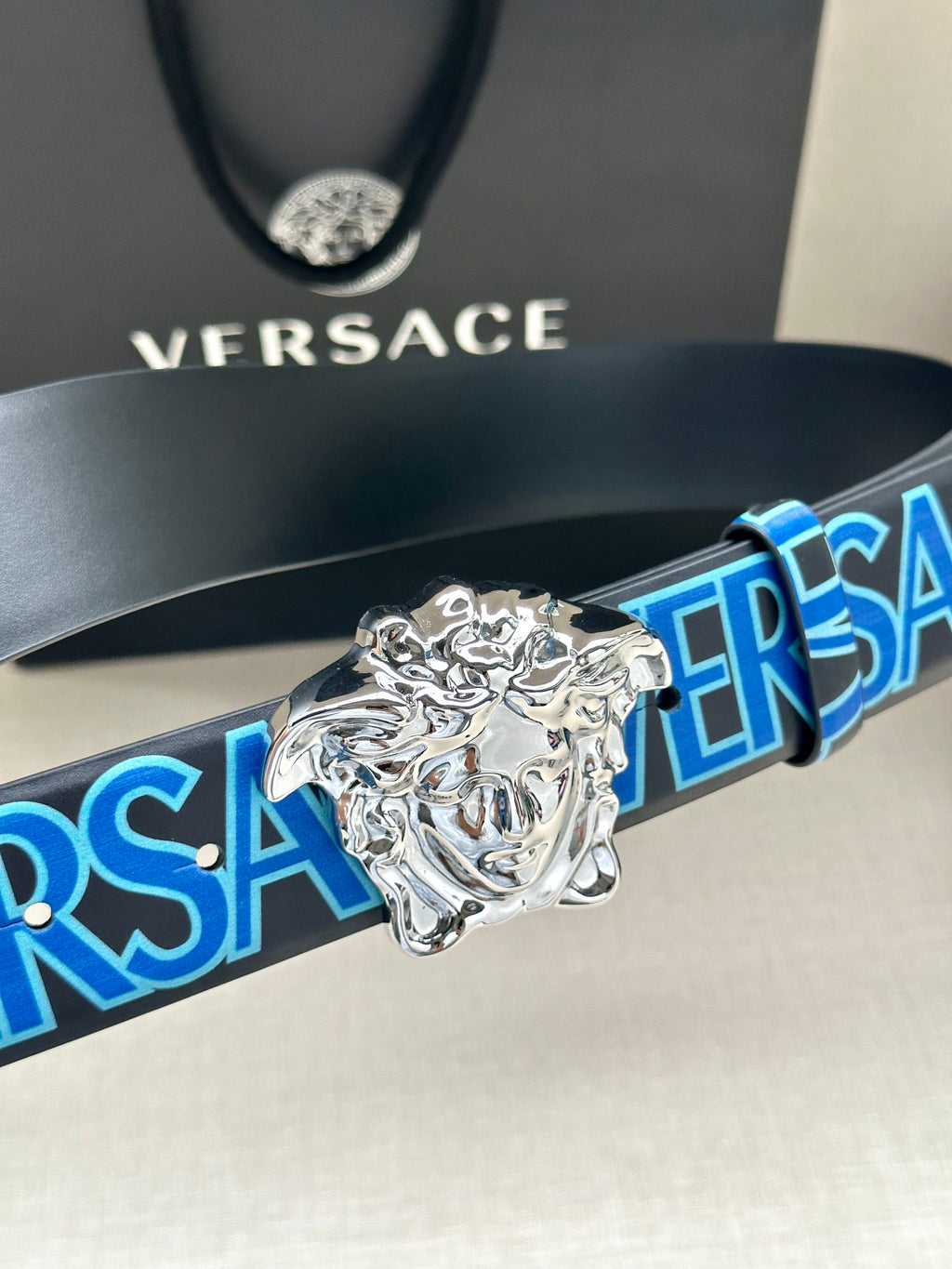 Versace belt detail with dark strap, blue logo pattern, and silver Medusa buckle