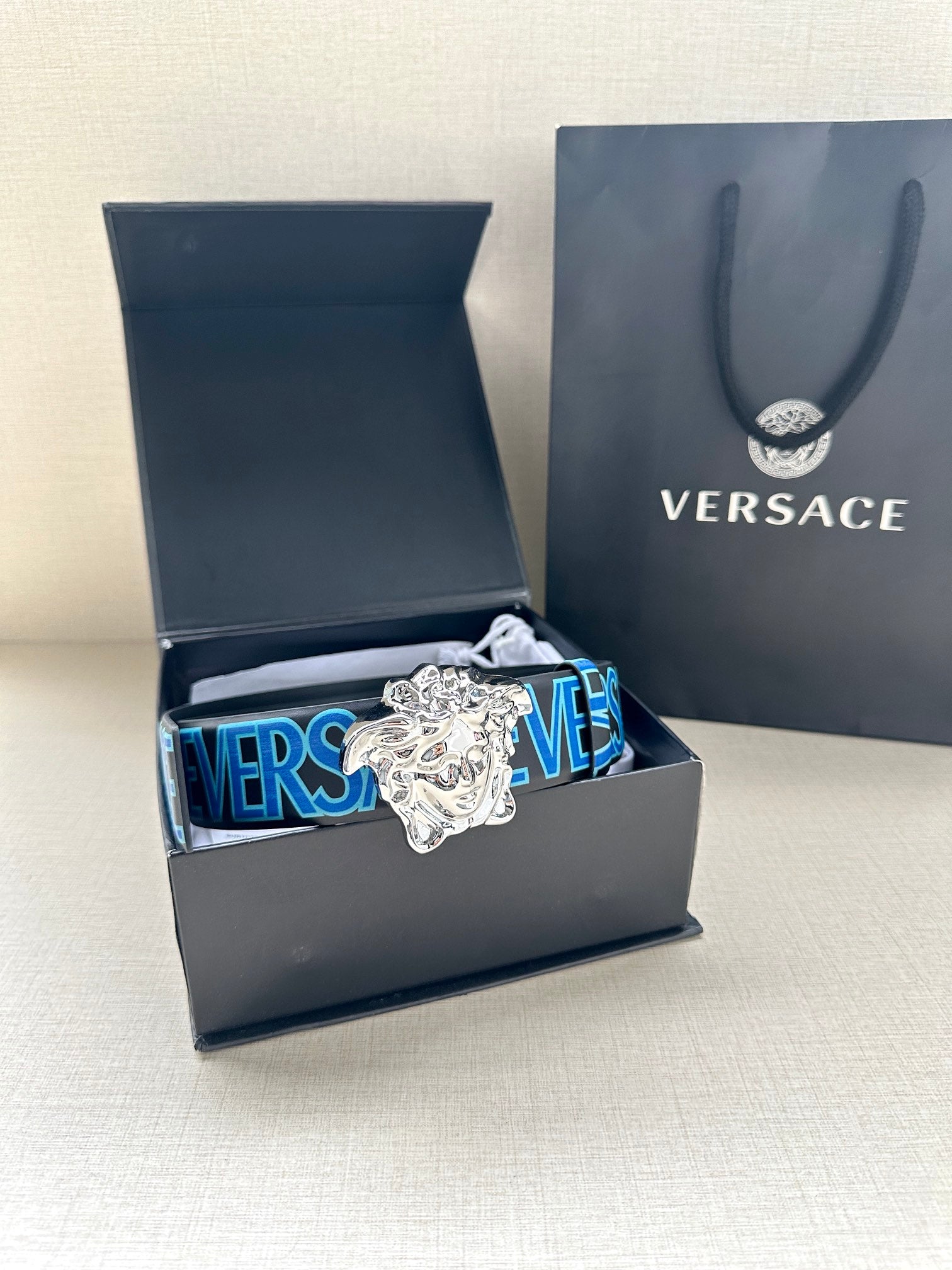 Versace belt displayed in gift box: dark strap, blue logo, silver Medusa buckle