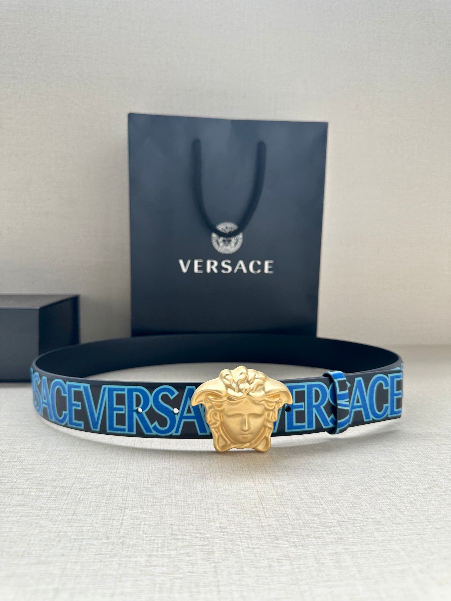 Versace belt with dark blue strap, repeating Versace print, and gold Medusa buckle.