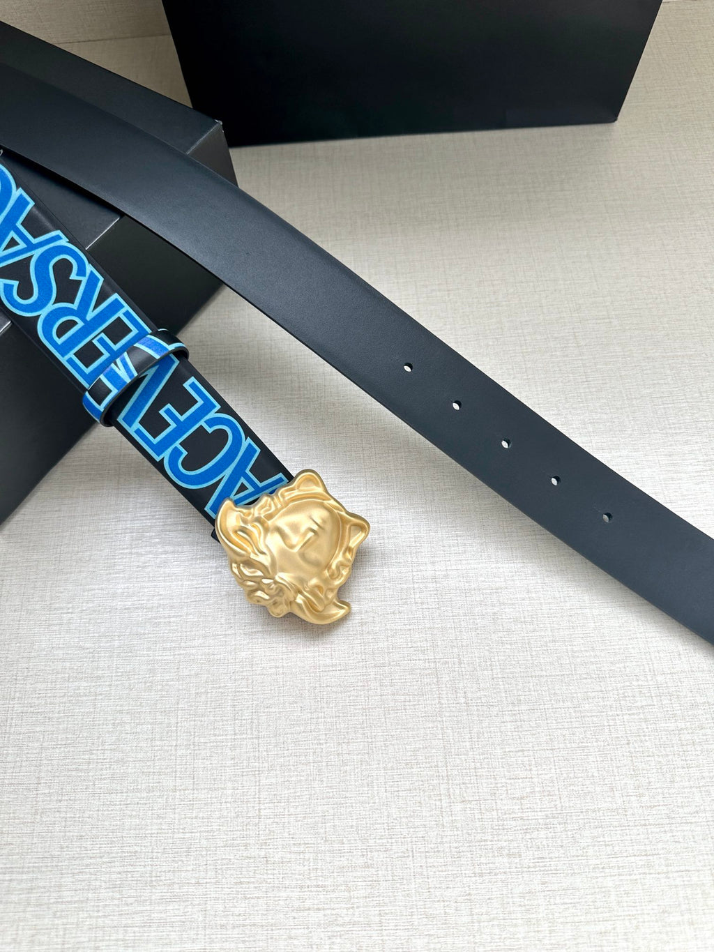 Versace belt close-up: dark blue strap with holes and gold Medusa buckle.