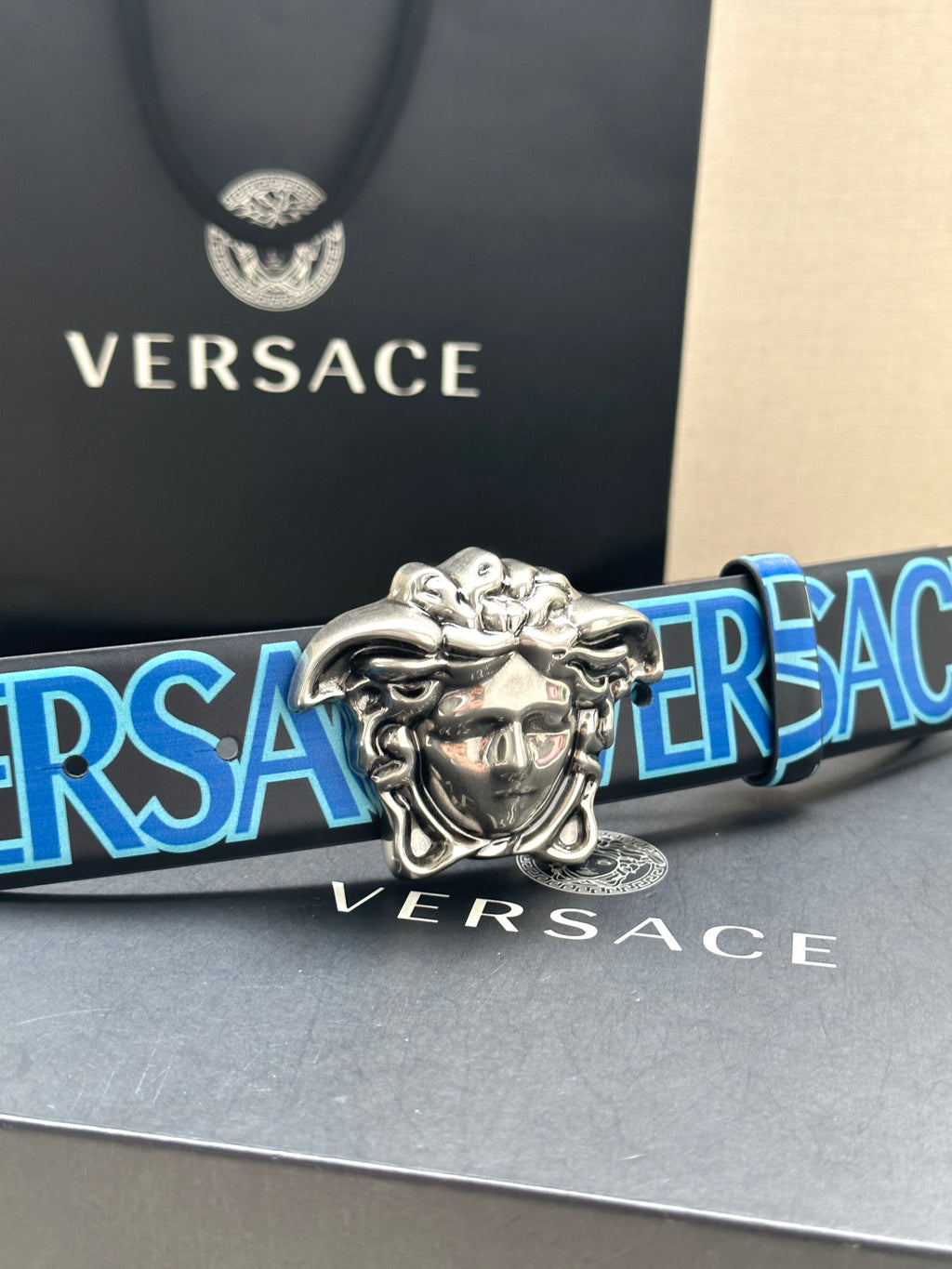 Versace belt close-up: blue logo strap and silver Medusa buckle