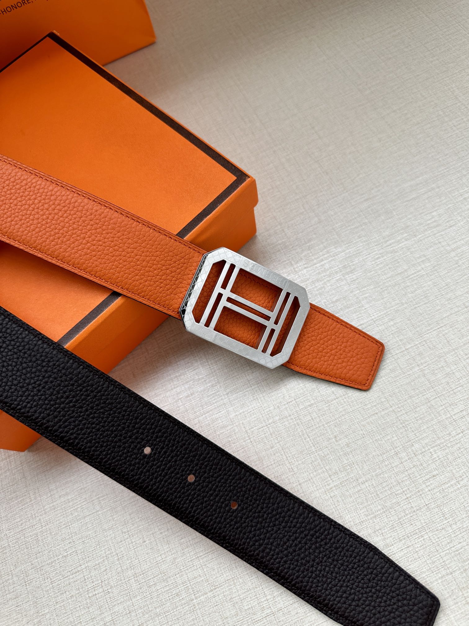 Hermes belt with orange strap and silver buckle, black keeper detail.