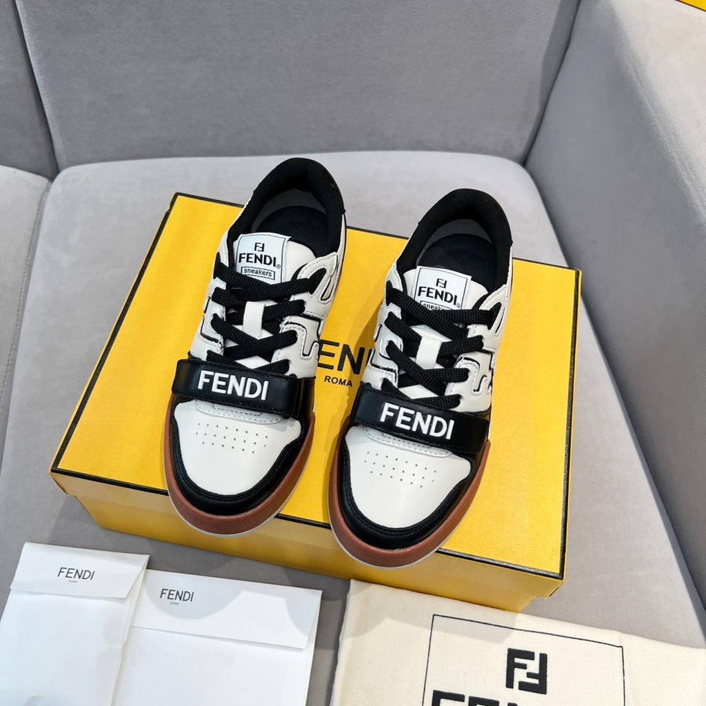 Two black-and-white low-top sneakers in a box, with lace-up straps and brown trim