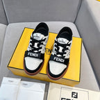 Two black-and-white low-top sneakers in a box, with lace-up straps and brown trim
