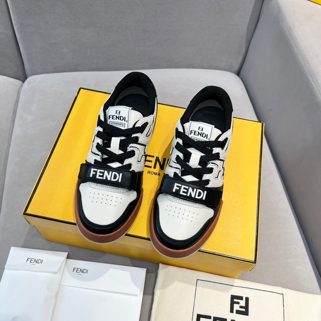 Two black-and-white low-top sneakers in a box, with lace-up straps and brown trim