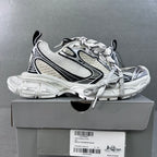 White chunky lace-up sneakers with black trim and textured sole on a box