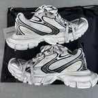White chunky lace-up sneakers with black stripe detailing, resting on a black bag