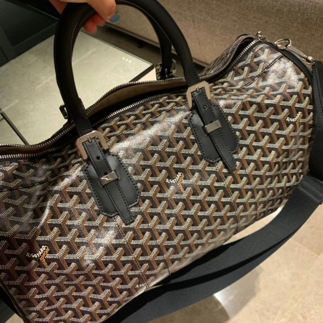Patterned duffel bag close-up with black leather straps and zip pulls