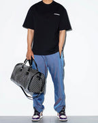 Patterned duffel bag with adjustable strap and dual top zippers, black leather trim
