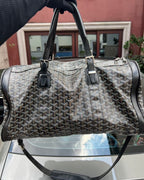 Patterned duffel bag with zippered top, black leather trim, two front strap tabs