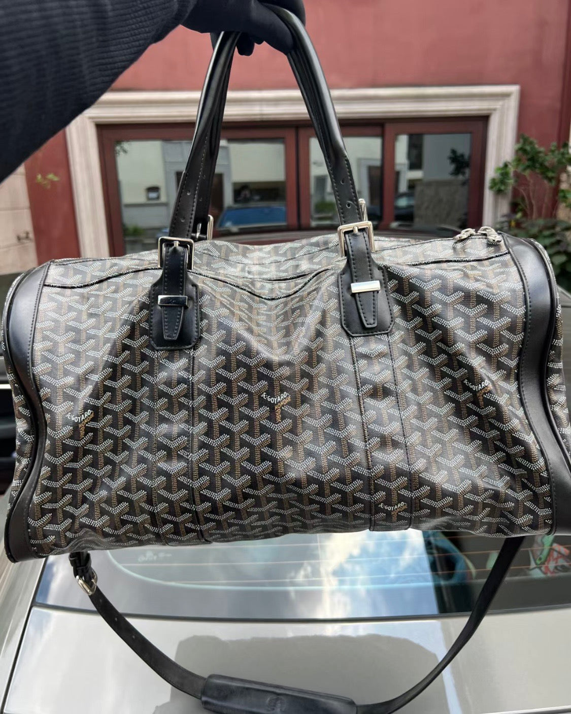 Patterned duffel bag with zippered top, black leather trim, two front strap tabs