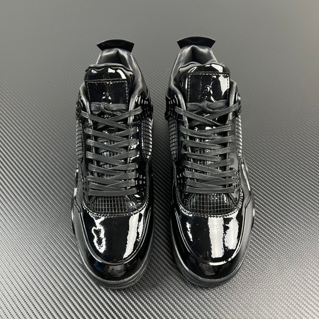 Pair of black Air Jordan 4 sneakers, glossy finish, lace-up with mesh overlays.