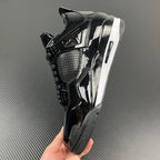 Black Air Jordan 4 sneaker in hand, glossy finish, perforated mesh panel.