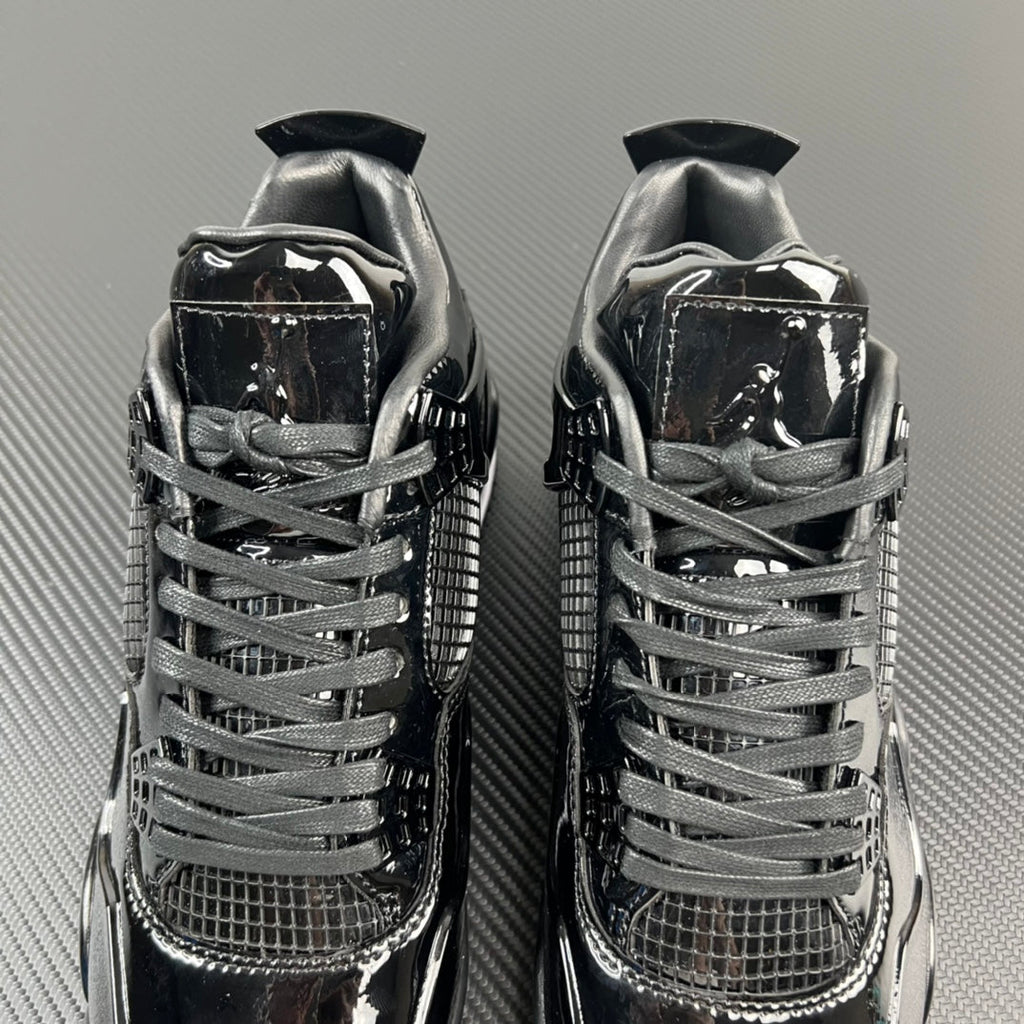 Two black Air Jordan 4 sneakers, lace-up uppers with mesh and patent panels.