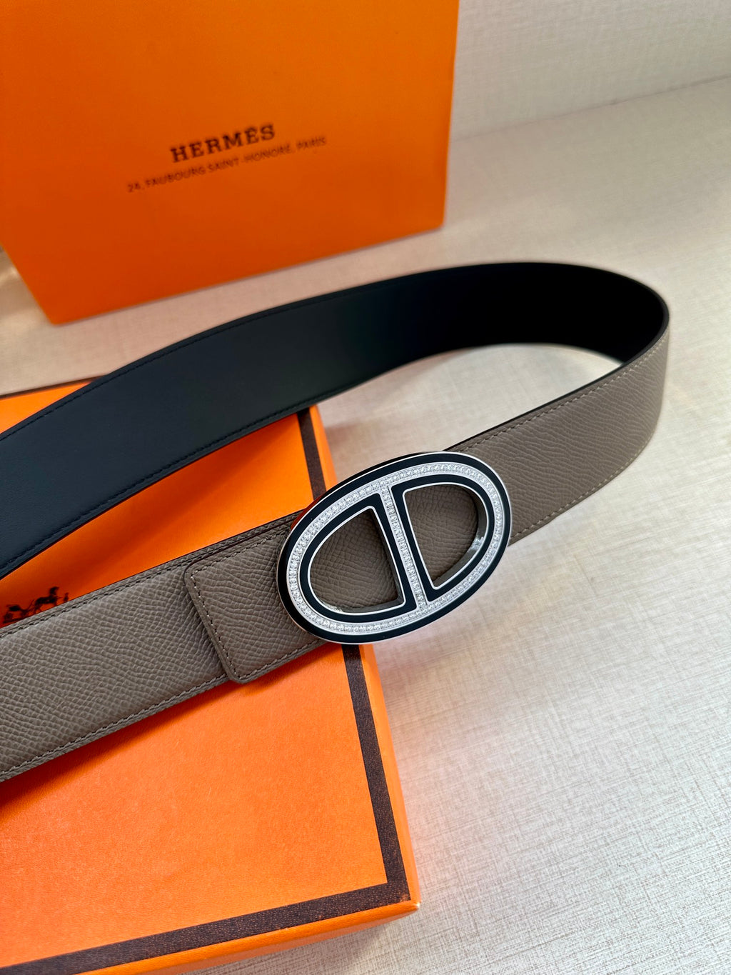 Gray leather belt with oval H buckle and silver-tone outer ring.