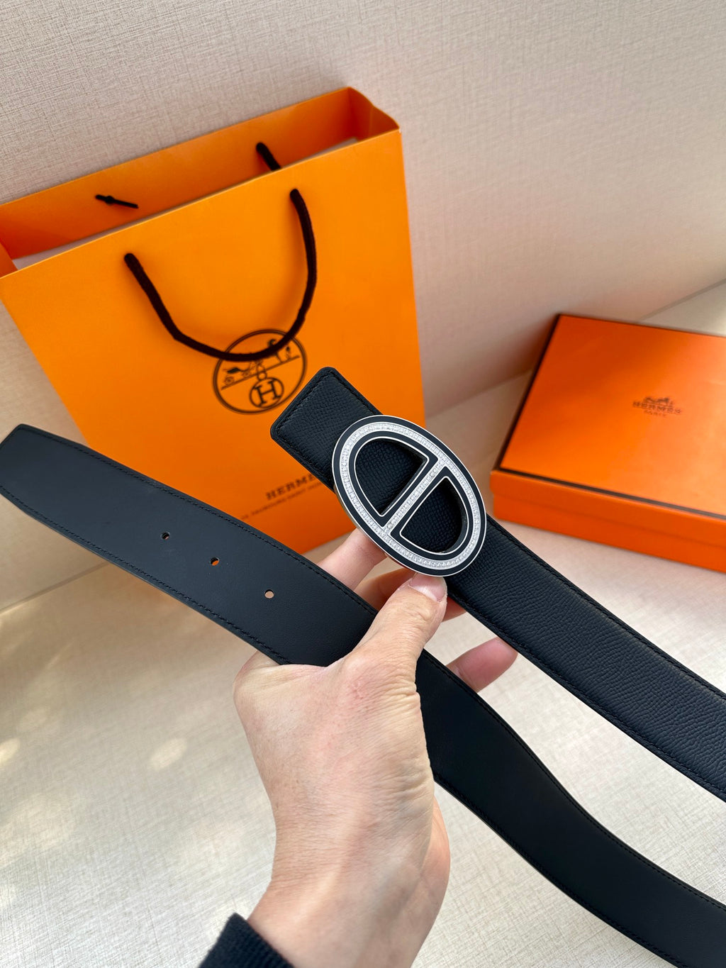 Black leather belt held up, featuring a silver-toned double “H” buckle and strap holes.