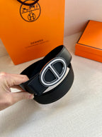 Black leather belt at an angle with silver-toned double “H” buckle and textured finish.
