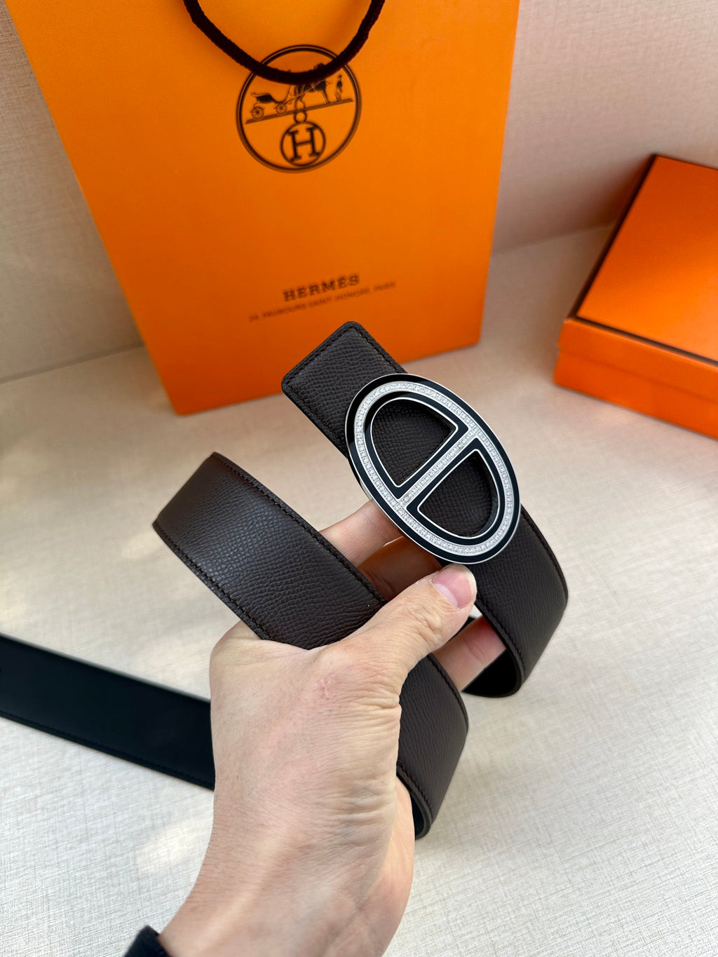 Black leather belt with silver double-H buckle, held in hand