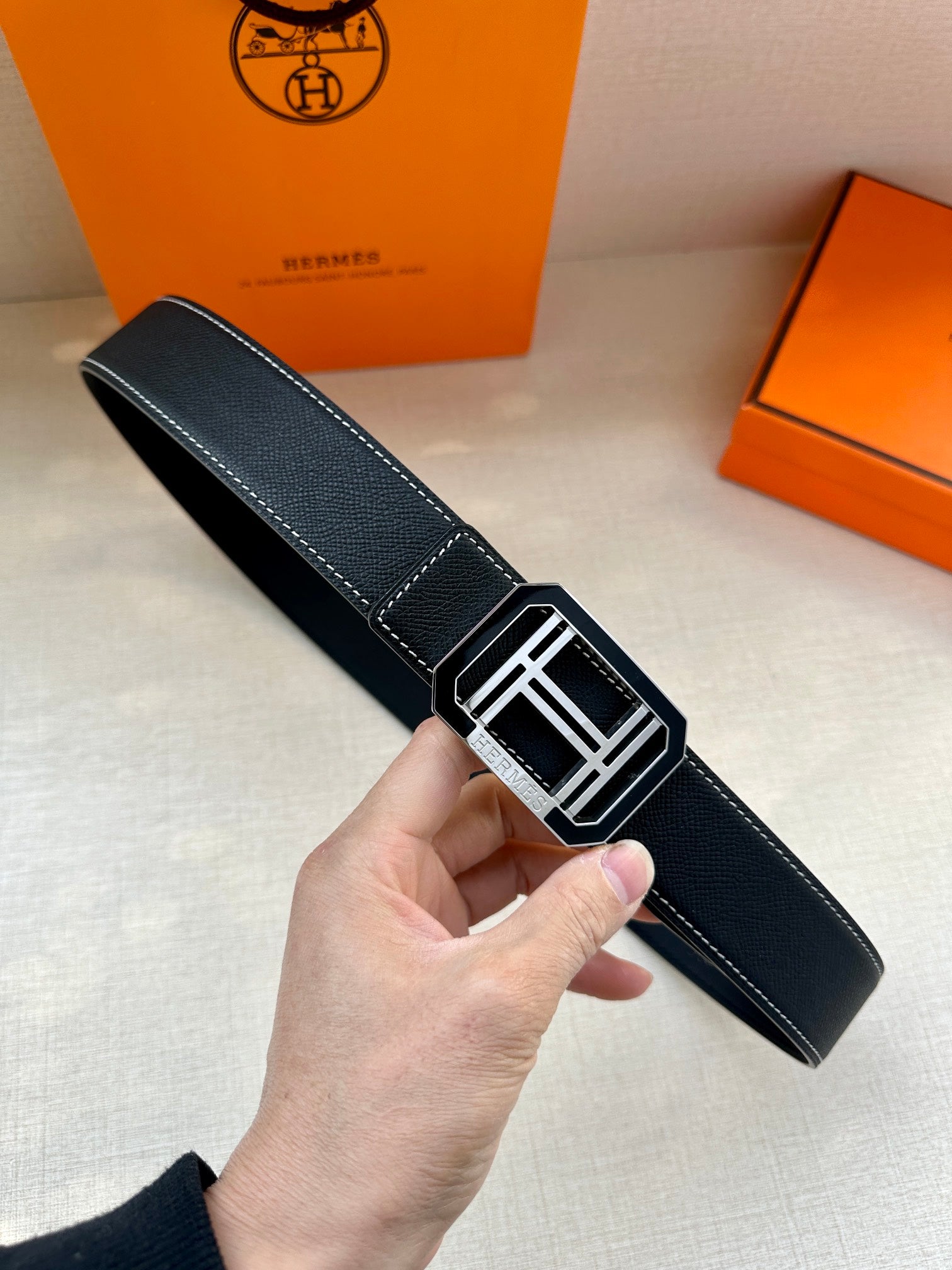 Dark leather belt with square silver-tone buckle and contrast white stitching.