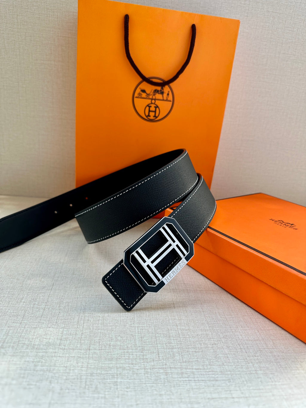 Dark leather belt with silver-tone square buckle and white contrast stitching, angled.