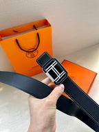 Dark leather belt held up, showing silver-tone square buckle and contrast white stitching.