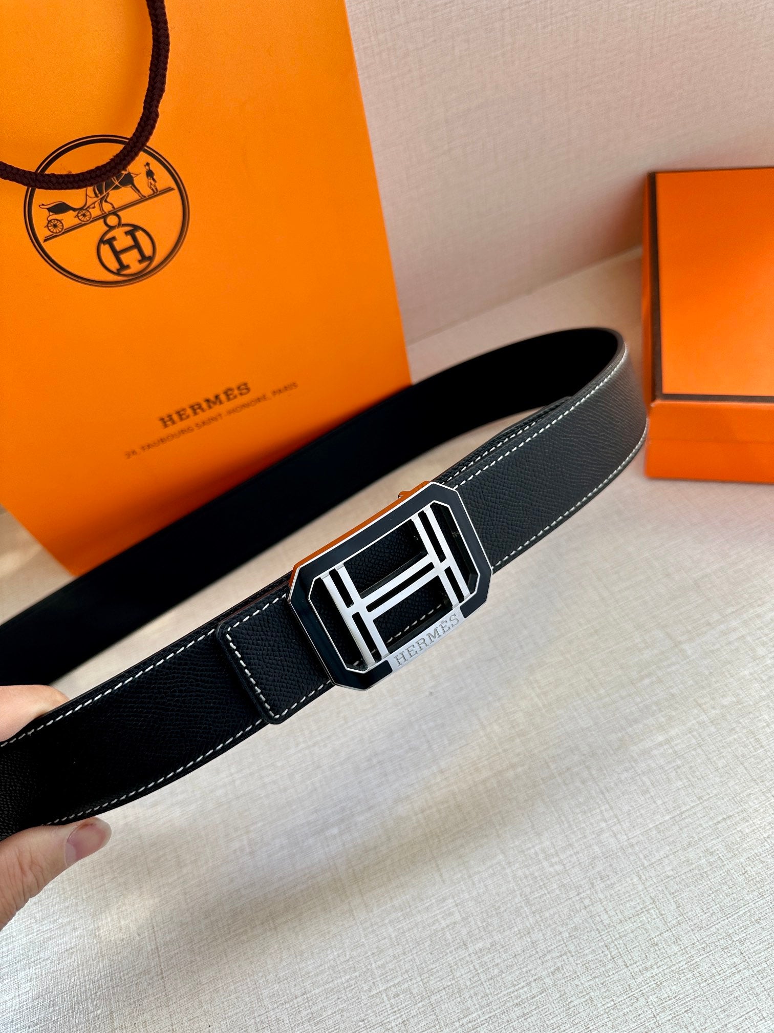 Dark leather belt close-up, featuring a silver-tone square buckle with white details.