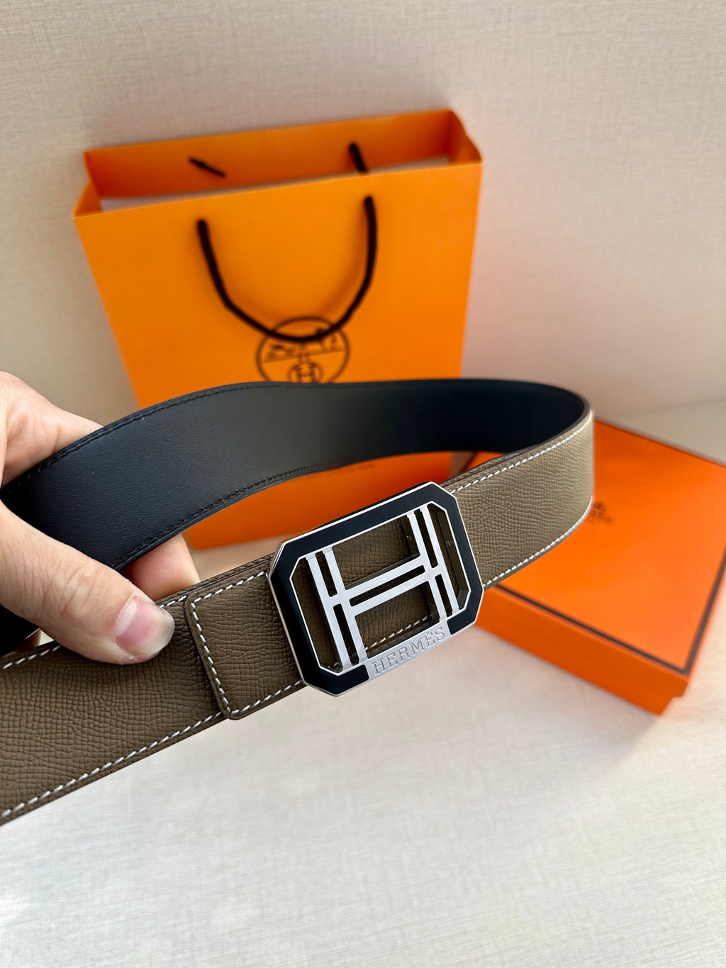 Leather belt with square H buckle, hand holding the strap end