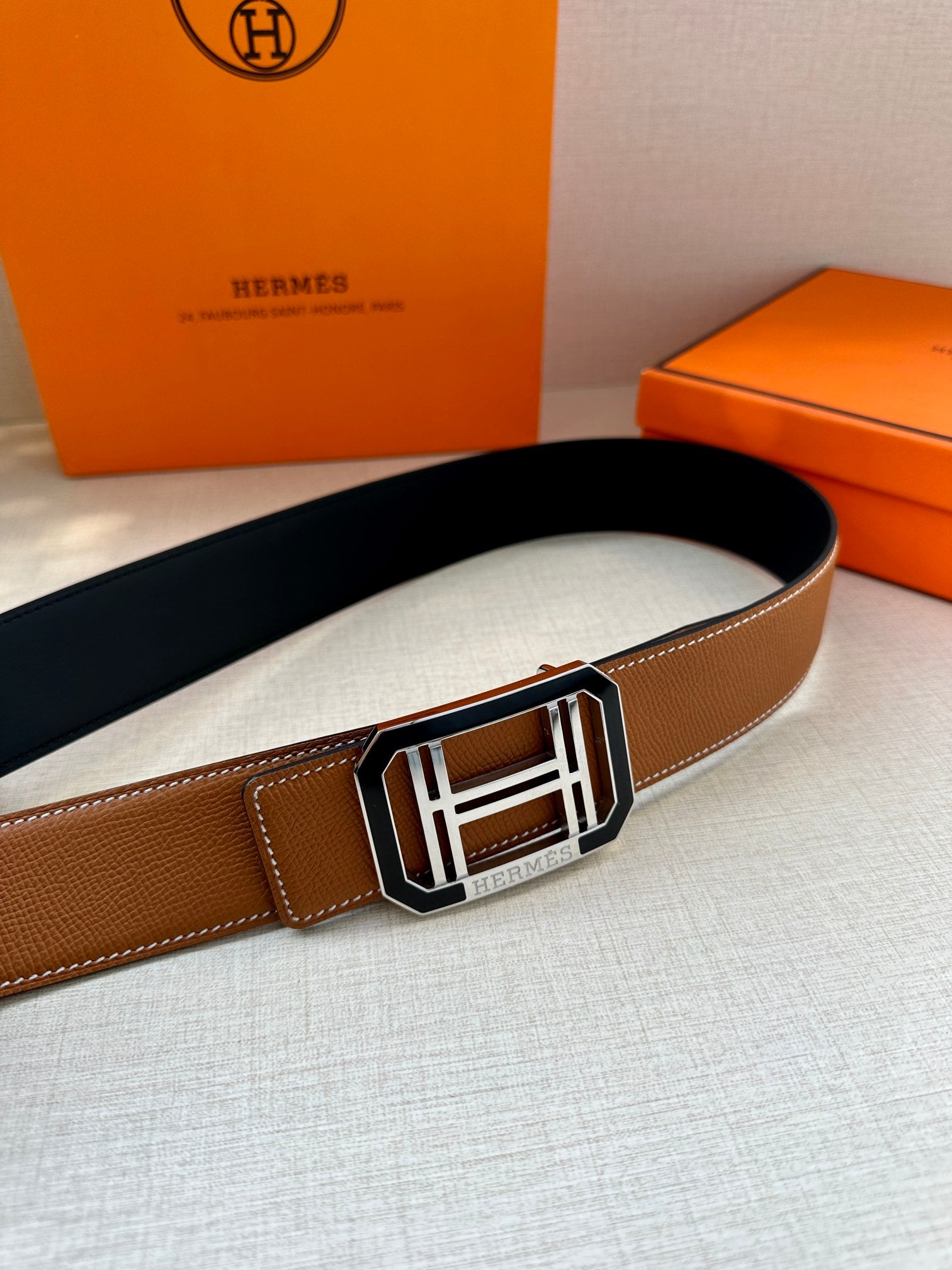 Tan Hermes belt with wide silver-and-black H buckle