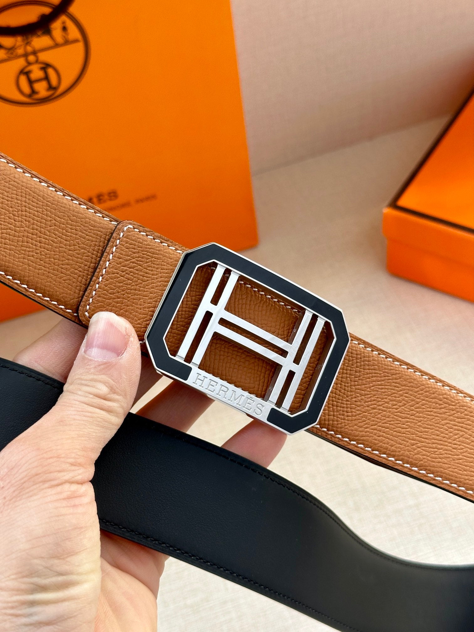 Close-up of tan Hermes belt with silver H buckle and stitched edge