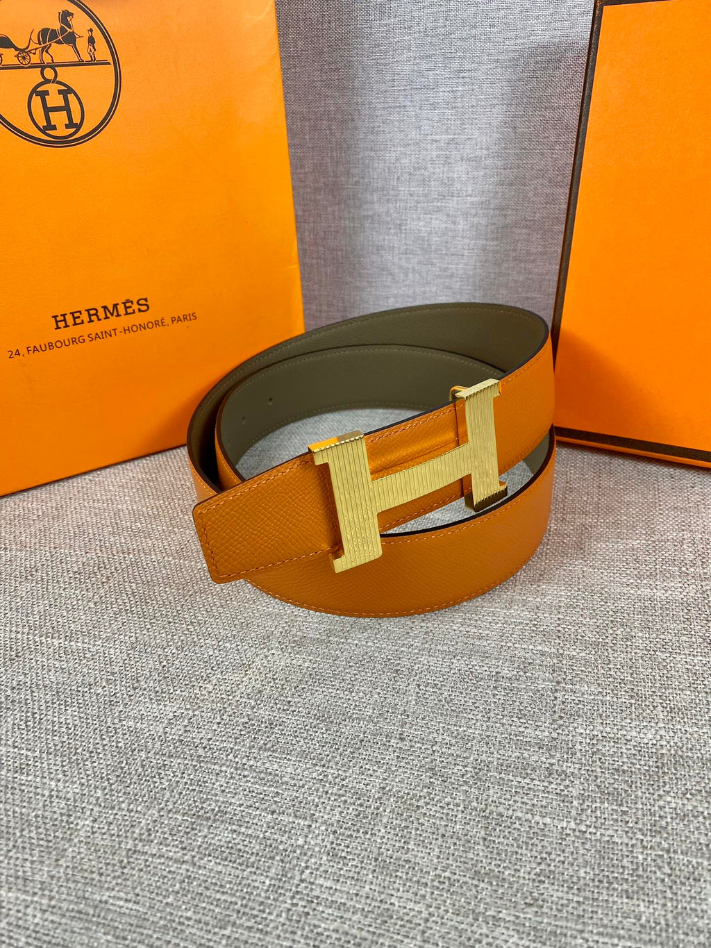Two-tone leather belt with wide orange strap, olive underside, and silver H buckle