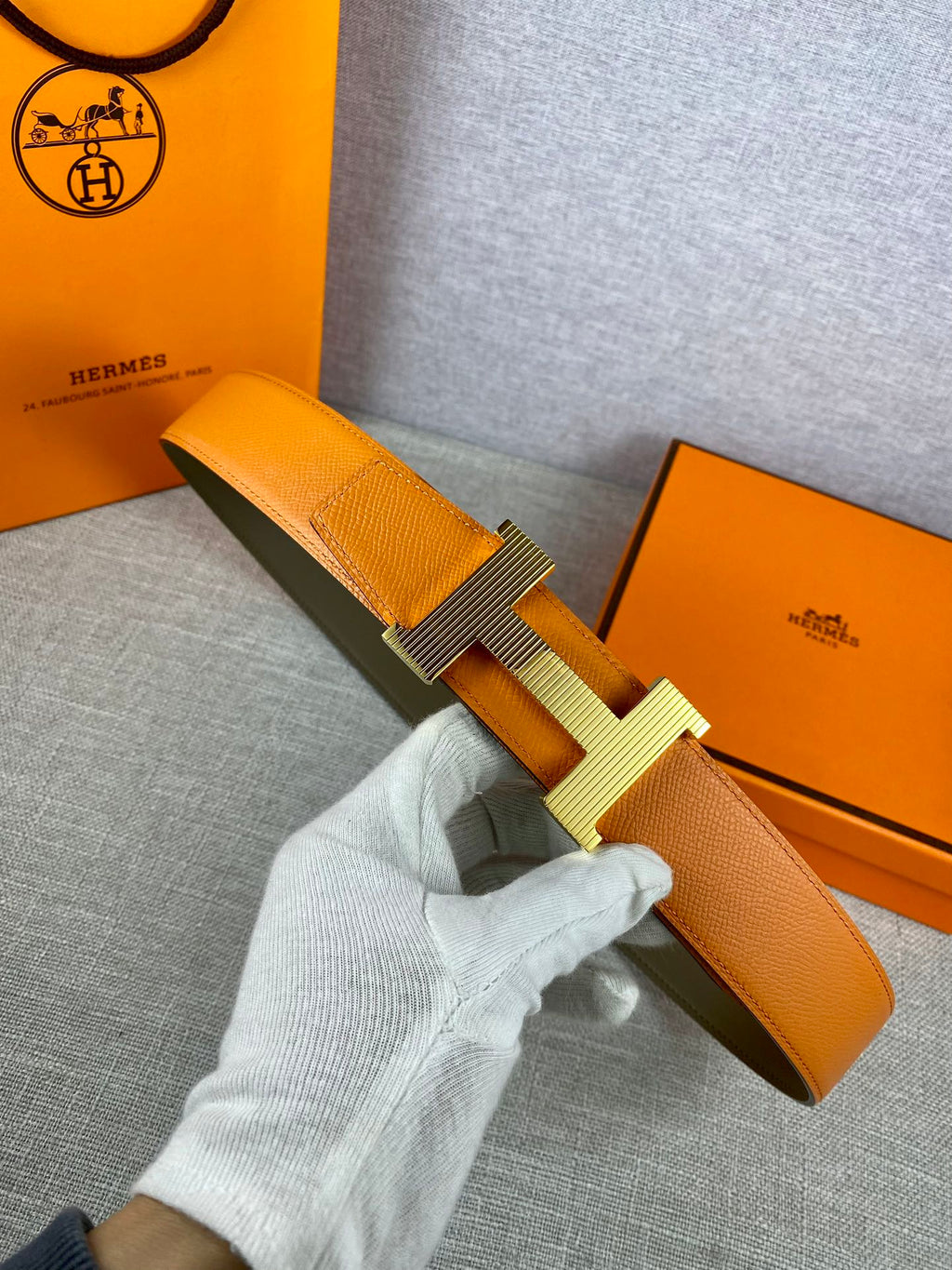 Two-tone leather belt with textured orange strap and light silver H buckle