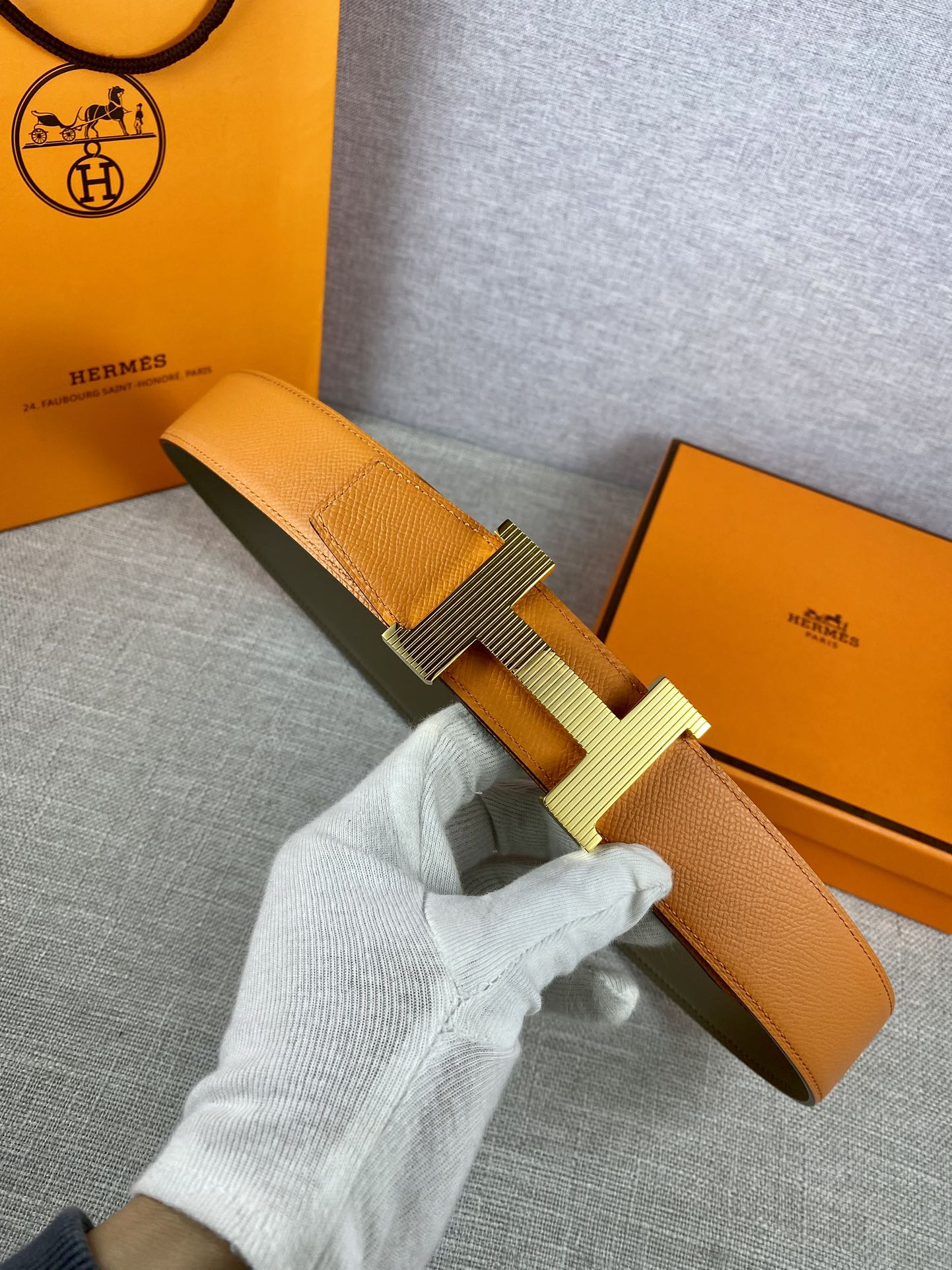 Two-tone leather belt with textured orange strap and light silver H buckle
