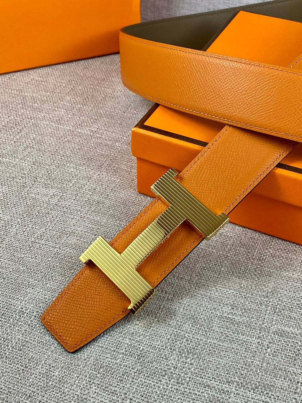 Two-tone leather belt with orange strap, olive backing, and H buckle detail