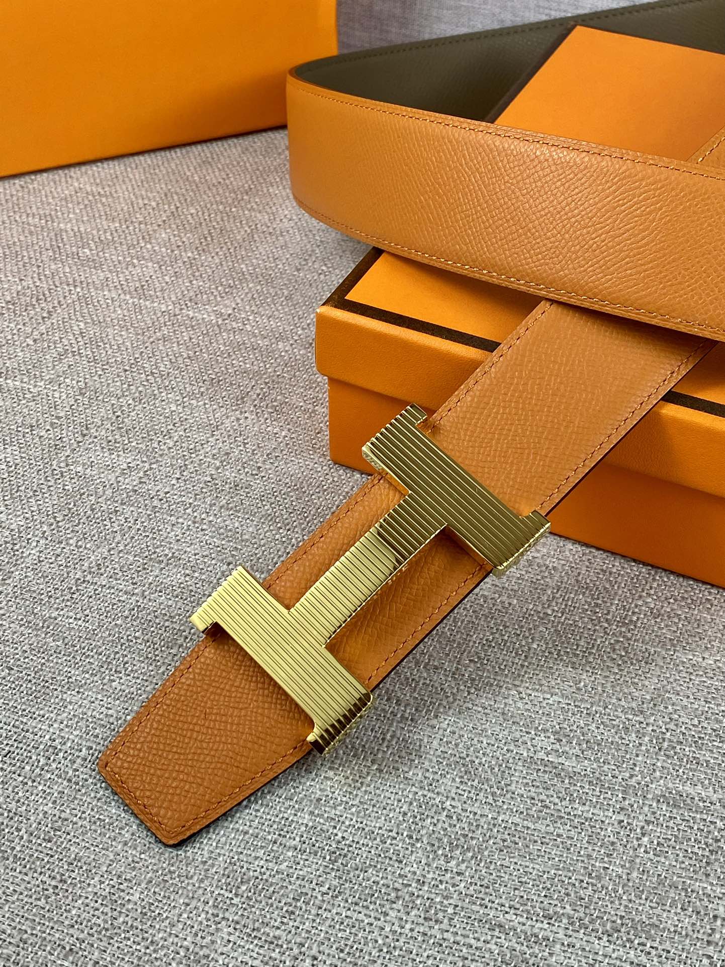 Two-tone leather belt with orange strap, olive backing, and H buckle detail