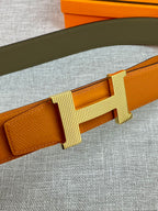 Orange leather belt with ribbed H buckle in light gold tone, close-up